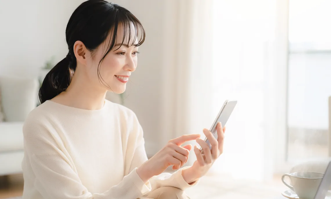 ソファでスマートフォンを見て届いたお知らせを確認する女性